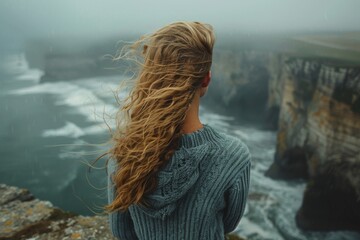 Melancholic atmosphere as a woman with windblown hair overlooks the formidable cliffs and turbulent...