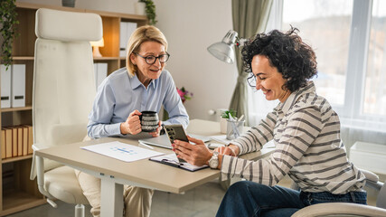 Two mature woman have coffee break at office