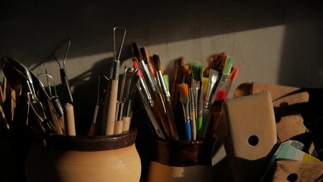 A close-up shot of paint brushes and modeling clay tools in ceramic vases.