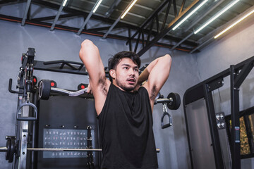 Fototapeta na wymiar A fit asian man does a set of EZ bar standing french presses. Training triceps and upper arms at the gym.