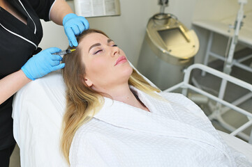 dermatologist cosmetologist performs a mesotherapy procedure and injects an injection into the scalp of a young woman patient.