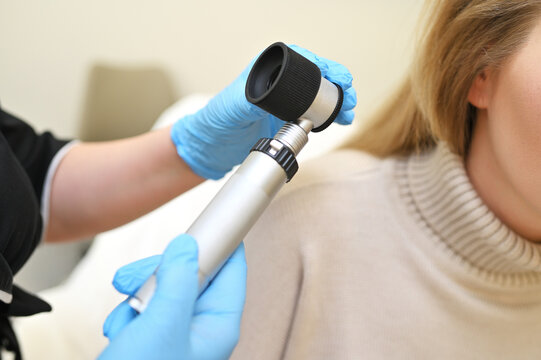 dermatologist trichologist examines the hair structure of a young woman's patient using an optical dermatoscope device.