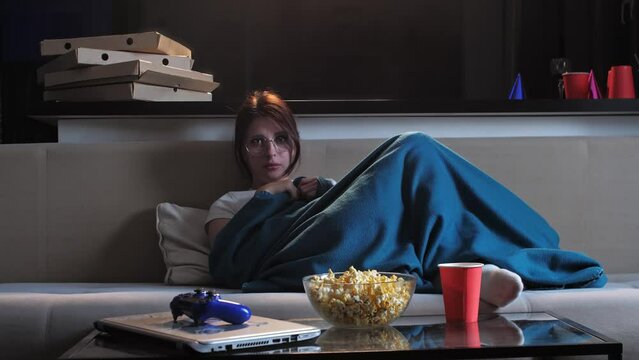 A young woman is watching a movie on the couch in her home, but she finds it difficult to stay awake and keeps falling asleep. Mid shot. 4k