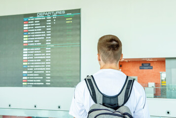 Young male traveler looking at airport departure board to check flight status and gate number