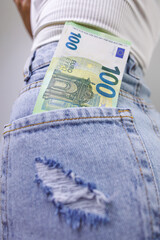 A close-up of a hundred euro bill sticking out of the back pocket of his jeans. A girl in jeans with a euro banknote in her hands.