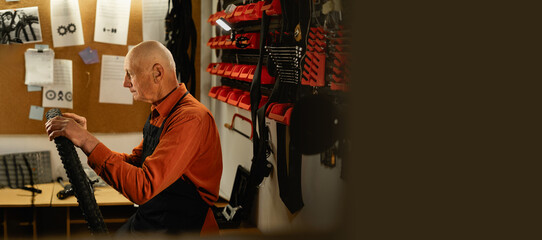 Male senior mechanic working in bicycle repair shop, old man repairing bike using special tool in...