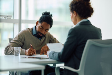 Black man signing agreement during  meeting with financial advisor in office.