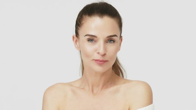 Happy mature middle-aged woman touching face and looking at camera. Healthy, dry skin care concept, cosmetics and anti-aging plastic surgery.