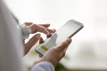 Aged female general practitioner holding modern smart phone in hands, close up screen view with...