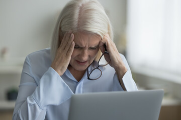 Close up woman sit near laptop take off glasses suffers from migraine, severe headache due to information overload, experiencing symptoms of eyestrain, blurry vision, feel stressed. Pressure, deadline