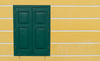 A green window with yellow trim sits in front of a yellow wall. The window is open, letting in a...