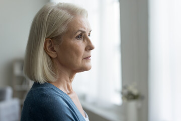 Close up portrait of serious upset older woman looking out window, lost in thoughts, think about problems, remember past, ponder future, feels depressed or lonely. Memories, melancholy, nostalgic mood - obrazy, fototapety, plakaty