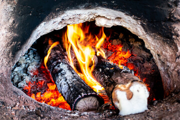 A fire is burning in a hole in the ground. The fire is surrounded by wood logs and the logs are...