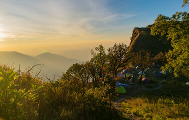 A group of tents are set up on a hillside, with a beautiful sunset in the background. Concept of...