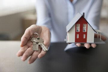 Unknown mature female hands holding bunch of keys and miniature of modern chalet house, close up....