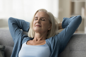 Close up portrait of calm middle-aged woman resting on couch with hands behind head, enjoy lazy weekend, meditating with eyes closed, feeling serenity, breathing fresh air, spend leisure time at home