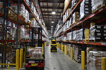 Forklift Operating in a Busy Warehouse Aisle with Stacked Goods and Shelves