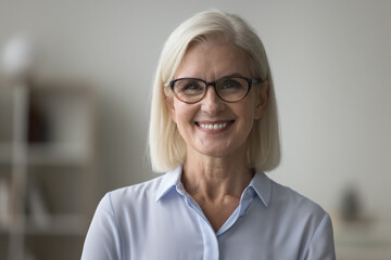 Head shot pretty smiling mature businesswoman in glasses and casual blouse posing indoor. Profile...