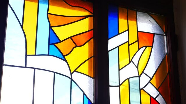 Colourful stained glass window with intricate designs in church. Sunlight filtering through ornate stained glass window. Depiction of religious figures in radiant stained glass window. 
