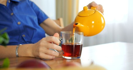 Pouring black Indian tea close-up, vibrant yellow teapot, cozy ambiance. Cinematic tea moment...