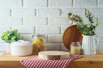 Empty wooden log  on kitchen table with food jars and plants over white brick wall  background. ...