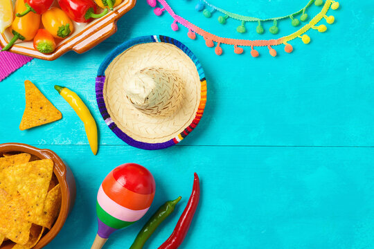Nacho tortilla chips, peppers, maracas and sombrero hat on blue wooden background. Mexican party Cinco de Mayo holiday celebration. Top view, flat lay