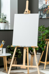 A white blank canvas on an easel with white flowers and greenery around on a plain background..Empty white board for the guest list or photo. empty white board for drawing