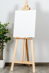 A white blank canvas on an easel with white flowers and greenery around on a plain background..Empty white board for the guest list or photo. empty white board for drawing - obrazy, fototapety, plakaty