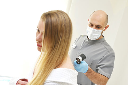 A dermatologist examines neoplasms on the patient's skin using a special dermatoscope device. Prevention of melanoma.