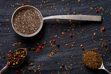 Old spoons with various seeds and spices on black background