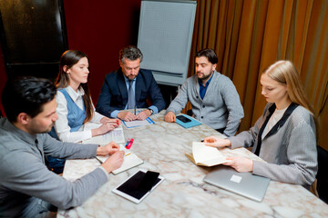 office workers are sitting in a conference room with red walls led by a director actively discussing