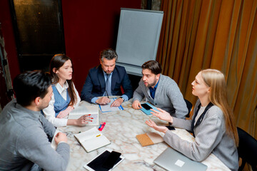 office workers are sitting in a conference room with red walls led by a director actively discussing