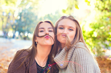 Fototapeta premium Fashionable beautiful young girlfriends with hairdress together in the autumn park background. Having fun and posing.
