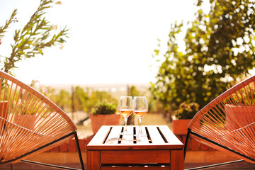 Glasses of white wine on rustic wooden table and flower pots on terrace outside
