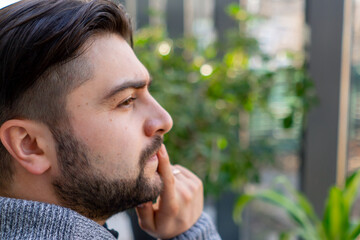 close-up of young guy with a beard thoughtfully looks out the window among the plants