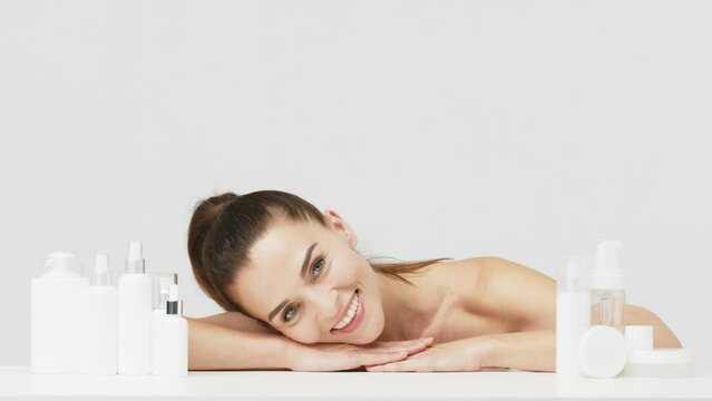 Portrait of a happy attractive middle-aged woman next to mock-ups of jars with cream and cosmetology natural cosmetics. Advertising of spa treatments, anti-aging care products for delicate dry skin.