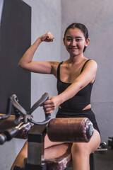 A young asian woman flexes her bicep before doing a set of v grip cable rows, training her back at the gym.
