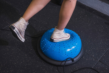 An anonymous young woman engaging in a core-strengthening workout as she balances on a Bosu Ball at the gym, focusing on fitness and stability.