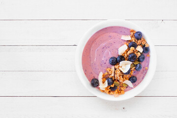 Healthy blueberry and coconut smoothie bowl with granola. Top view on a white wood background. - 783868987