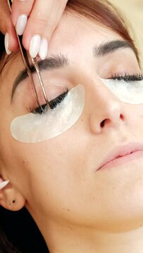 4k vertical high angle view video of beautician putting lashes extension to a beautiful woman. Close up. Stickers on eyebags. Unrecognizable hands from beautician.