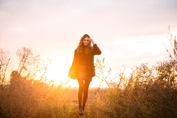 Young happy caucasian brunette woman walking through grassy meadow at sunset and smiling