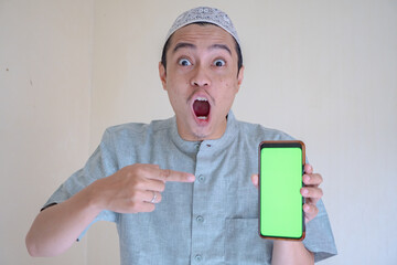 Moslem Asian man surprised gesture show the greenscreen on smartphone when Ramadan celebration. The photo is suitable to use for Ramadhan poster and Muslim content media.