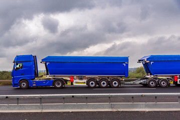 Truck with two semi-trailers attached, commonly called Duo-trailer, traveling on a highway, side view.