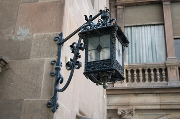 Detail of an old and ornate wrought iron lamp placed in the corner of a stone facade with an angled...