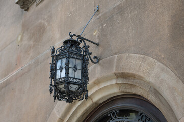Detail of an old and ornate wrought iron lamp hanging above the entrance of an old stone house in...