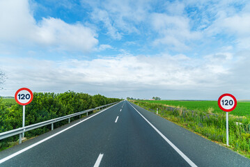 View of a straight highway that disappears into the background bordered by green fields under a...