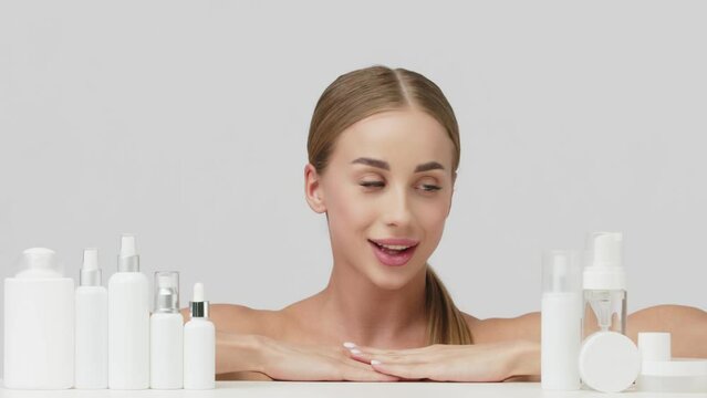 Nice woman on a white background among jars, bottles and tubes for cosmetic procedures. Production of natural cosmetics. Cosmetics based on natural ingredients, scrub, tonic, body care.