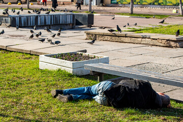 Drunk man sleeping on the grass under a bench on a city street