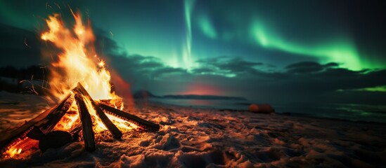 night landscape with a bonfire burning on the beach at sunrise and a northern lights in the sky.	