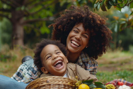 A woman and a child are laying on the grass, smiling and laughing. The woman is holding a basket of fruit, and the child is looking at her with a big smile on his face. The scene is joyful
